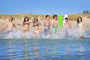 Teen surfers boys and girls group running happy to the beach splashing water