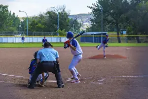 Teenage baseball batter waiting for the pitch while the pitcher is throwing the ball during a sunny summer game