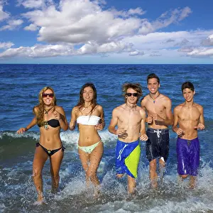 Teenagers group running happy splashing on the beach in summer vacations