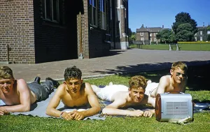 Four teenagers sunbathing on the lawn with a portable transistor radio, Melbourne Grammar School, Victoria, Australia 1956