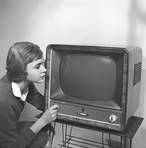 Television in the 1950s. A young woman is pictured beside a typical 50s television set. A Grundig tv standing on a typical metal string boned tv table. Kristoffersson ref CC93-2. Sweden 1958