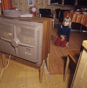 Television in the 1960s. A girl is sitting in front of a television set with her eyes on the screen and the program