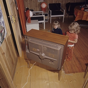 Television in the 1960s. Two girls are sitting in front of a television set with her eyes on the screen and the program