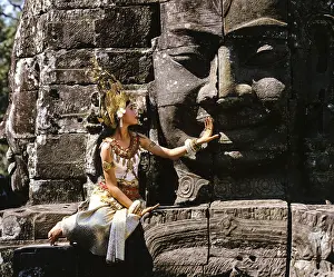 Temple dancer or apsara sitting in front of a face tower at Bayon Temple