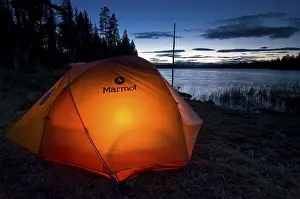 Tent illuminated from the inside at dusk on a lakeside