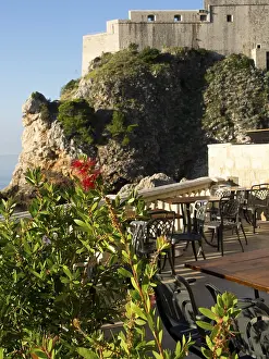 Terrace with chairs and tables next to a rock formation with sea view and historic fortress