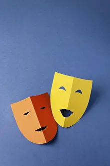 Two theatrical masks made of colored paper on a blue background