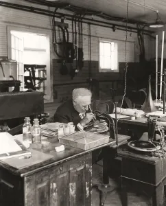 Thomas Alva Edison examining a phonograph disc under a microscope