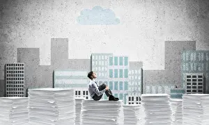 Thoughtful businessman looking away while sitting on pile of documents with drawn cityscape on background