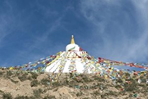 Tibetan Buddhism, white stupa with colorful prayer flags against a blue sky