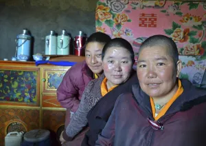 Three Tibetan nuns sitting in the kitchen of the nunnery in front of thermos flasks for the butter tea