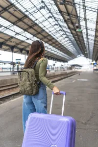 Tourist wearing headphones and carrying luggage strolls through a bustling train station