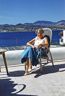Touristin mittleren Alters sitzt in der Sonne auf einer Terrasse am Meer, Insel Ibiza, Balearen, Spanien, 1950er Jahre