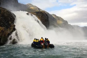 Tourists in rubber dinghy in front of waterfall