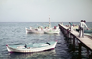 Tourists on the shore on the pier with a view of a fishing boat, Kos, Greece 1970s