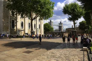 Tourists strolling near Tower Bridge under sunny skies with lush greenery at The Tower of London