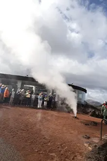Tourists watch steam rise from geyser spout