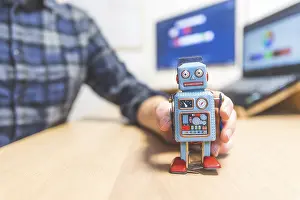 Toy robot on a desktop, man working on the computer in the background