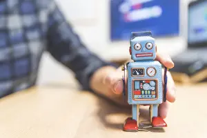 Toy robot on a desktop, man working on the computer in the background