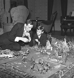 Toys in the 1940s. A man and his son on the floor playing with figures of cowboys and american indigenous people