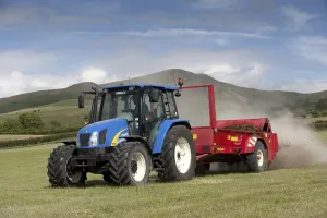 Tractor with muckspreader, spreading chicken manure mixed with lime on newly harvested meadow