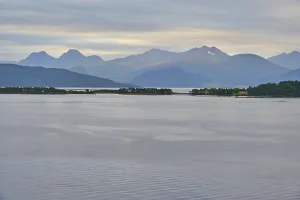 A tranquil fjord landscape with mountains in the background and islands covered by a cloudy sky