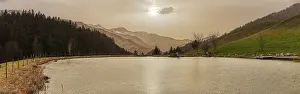 A tranquil lake against a mountain backdrop at sunset with trees and a gentle sky