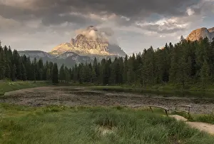 A tranquil scene with a mountain and a forest reflected in a calm lake (Lago Antorno) at sunset with some clouds