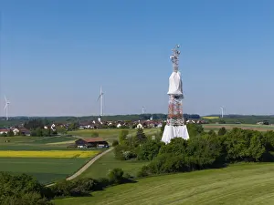 A transmission tower and wind turbines near a village under a blue sky