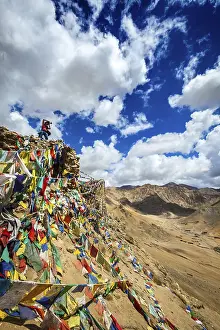 Travel photographer taking photos in Himalayas mountains on cliff with Buddhist prayer flags