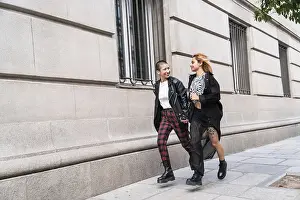 A trendy lesbian couple walks hand in hand along a city street