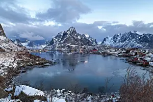 Twilight over a snowy village in Lofoten with calm waters and mountain backdrop