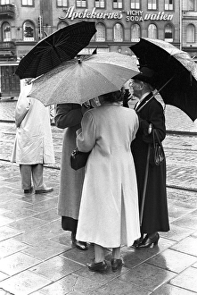Umbrellas in the 1950s. A group of elderly women are standing together under their umbrellas