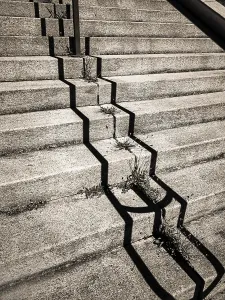 Uneven concrete steps in an urban area expose cracks filled with weeds growing in the crevices