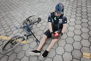Unhappy cyclist sitting on the pavement with knee pain