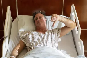 Unhappy patient in hospital bed giving thumbs down