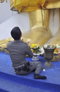 Uniformed police officer praying at the giant feet of a golden statue