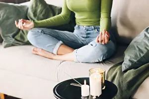 Unrecognizable barefoot woman sitting on bed in Lotus pose and meditating during yoga session at home