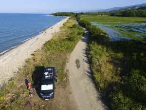 A van parked on a beach along a coastal road with lush vegetation and sea view