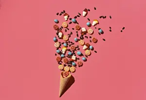 A variety of delicious sweets explode from the waffle cone on coral background