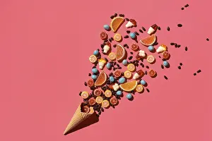 A variety of delicious sweets explode from the waffle cone on coral background