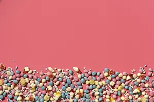 Various sweets, candys are palced on the bottom part of the photo on the coral background