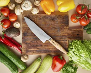 Vegetables around wooden cutting board with knife on kitchen table