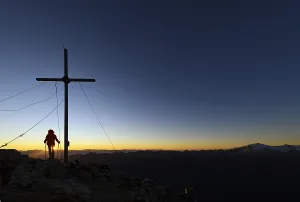Vermoispitze summit cross with climber at sunrise with South Tyrolean mountains in the background