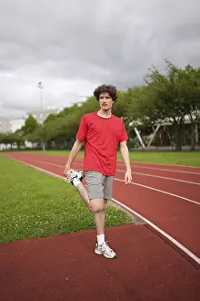 Vertical full length of a young male caucasian runner stretching the legs in running track