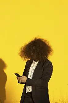 Vertical portrait of unrecognizable long-haired businessman with cellphone over yellow background