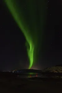 Vertical stream of green aurora over dark hills