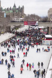 A vibrant crowd skates along a snowy frozen Rideau Canal in a festive urban setting in Ottawa