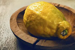 A vibrant lemon sits on a rustic wooden plate