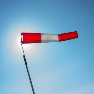 A vibrant windsock attached to a pole is fluttering in the wind against a clear blue sky